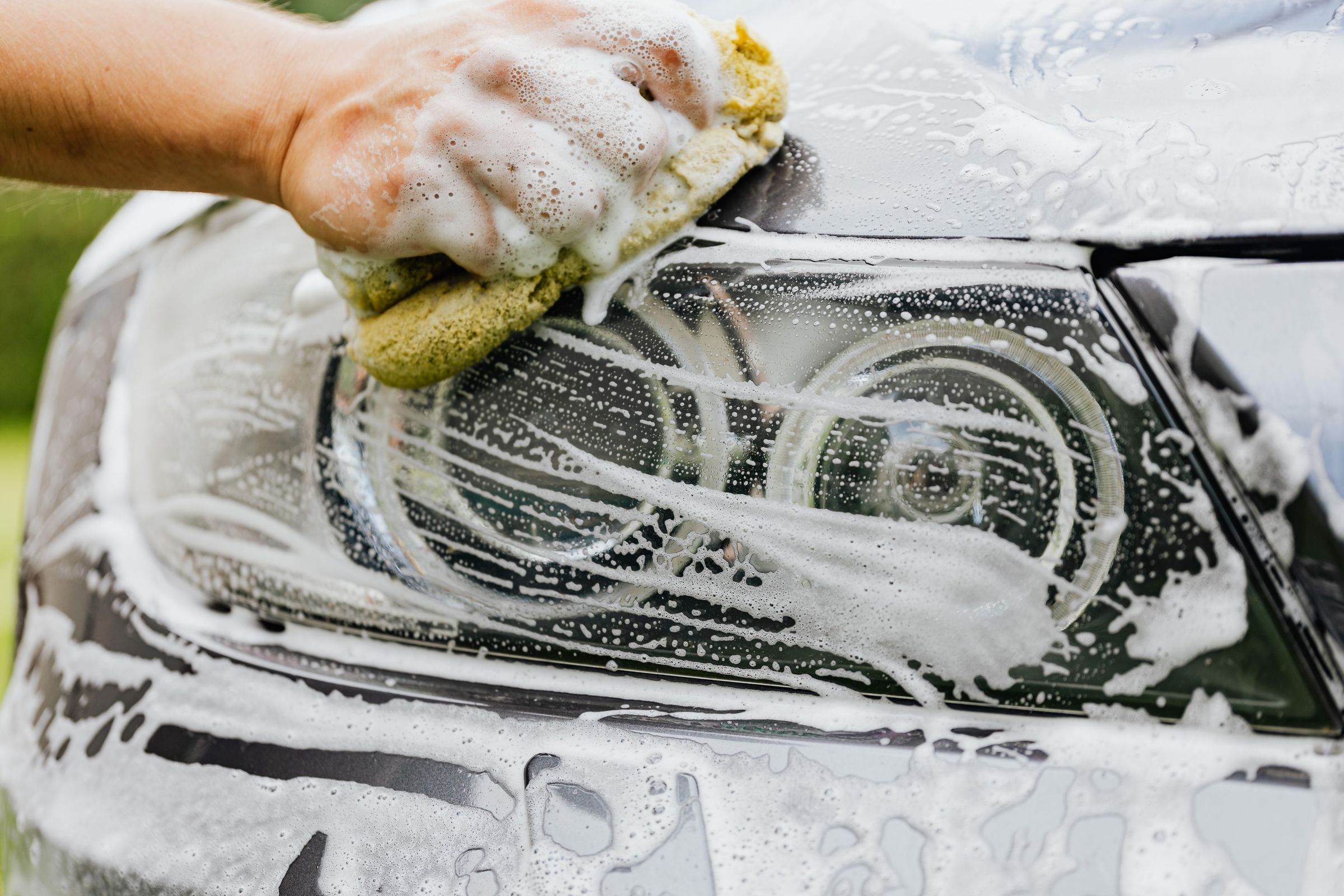 A headlight being scrubbed with a soapy sponge